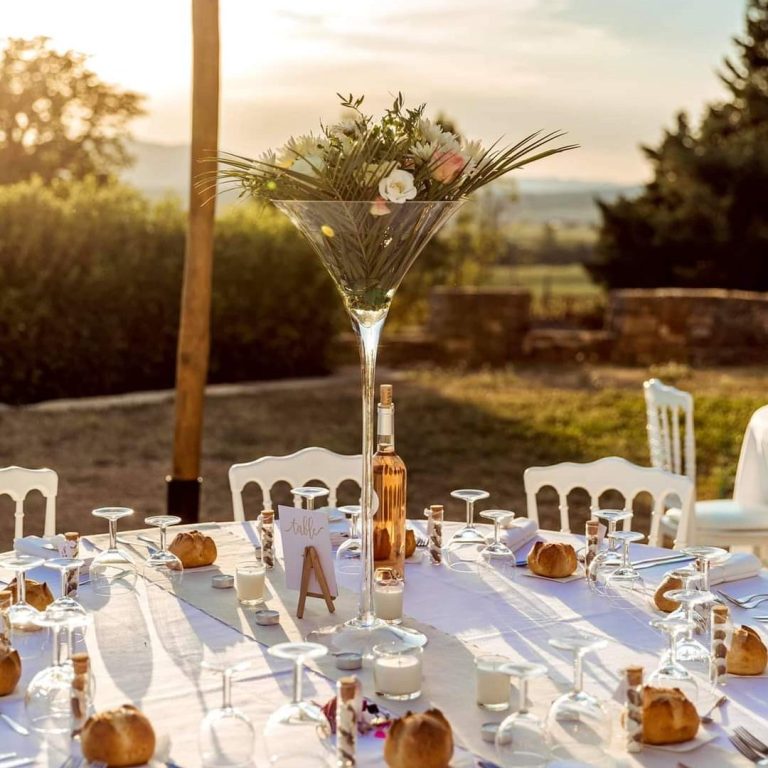 Table dressée avec des fleurs, croissants et couverts, vue sur un paysage ensoleillé.
