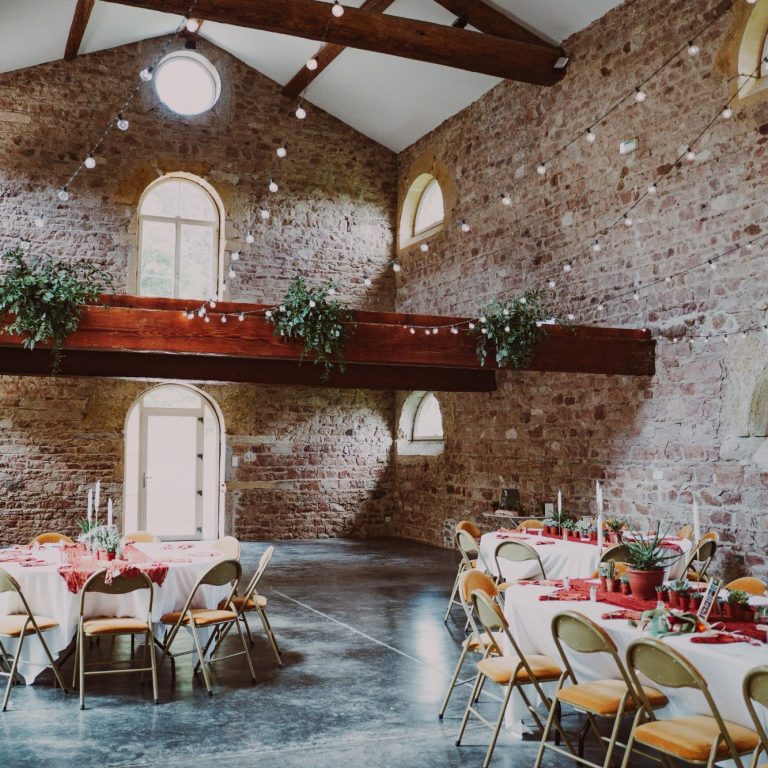 Salle de réception avec des tables décorées sous un plafond en bois et des murs en briques.
