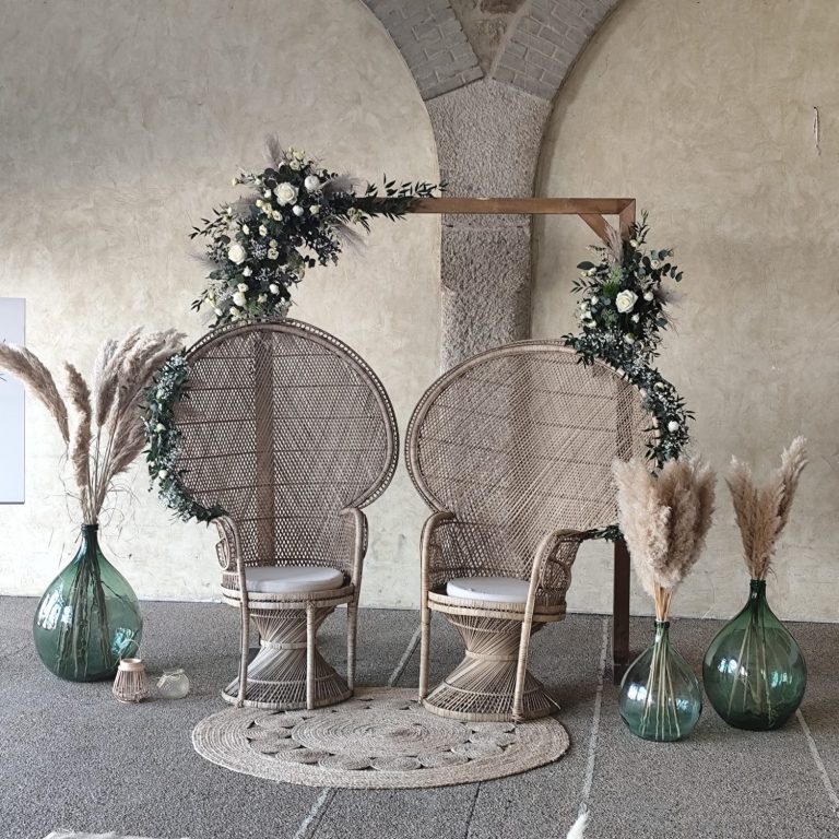 Deux chaises tressées avec des décorations florales et des vases en verre sur fond neutre.