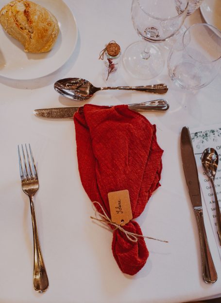 Serviette rouge nouée avec étiquette, accompagnée de couverts sur une table dressée.