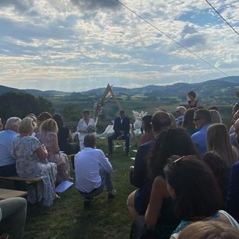 Cérémonie en plein air avec des invités devant un décor naturel et des montagnes en arrière-plan.