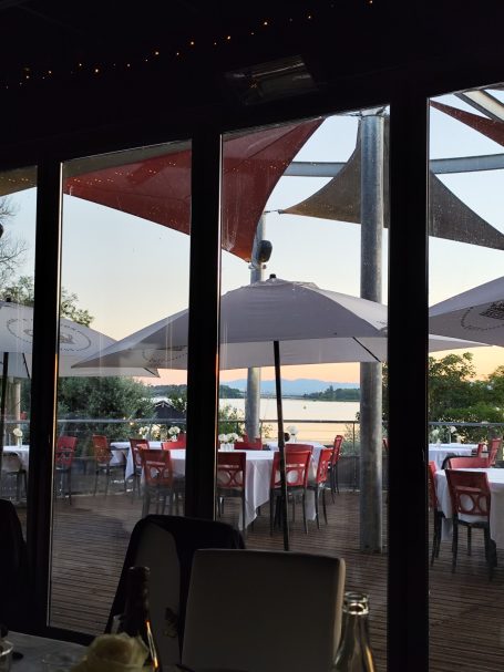 Terrasse de restaurant au bord de l'eau avec parasols et tables dressées.
