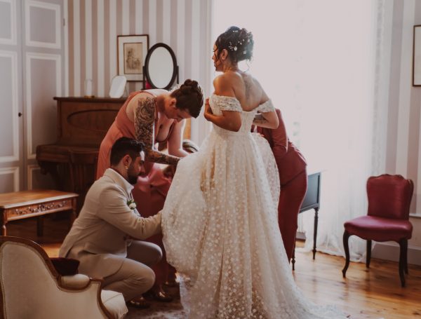 Mariée en robe blanche, entourée de proches dans une pièce élégante et lumineuse.