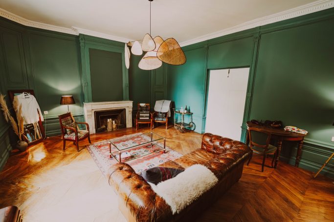 Salon spacieux avec murs verts, canapé en cuir et décoration vintage élégante.