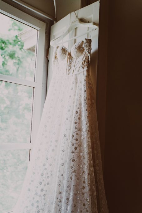 Robe de mariée blanche élégante suspendue près d'une fenêtre avec lumière naturelle.